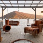 Covered lakeside deck with wicker furniture and a clay chiminea overlooking a mountain lake at sunset in autumn